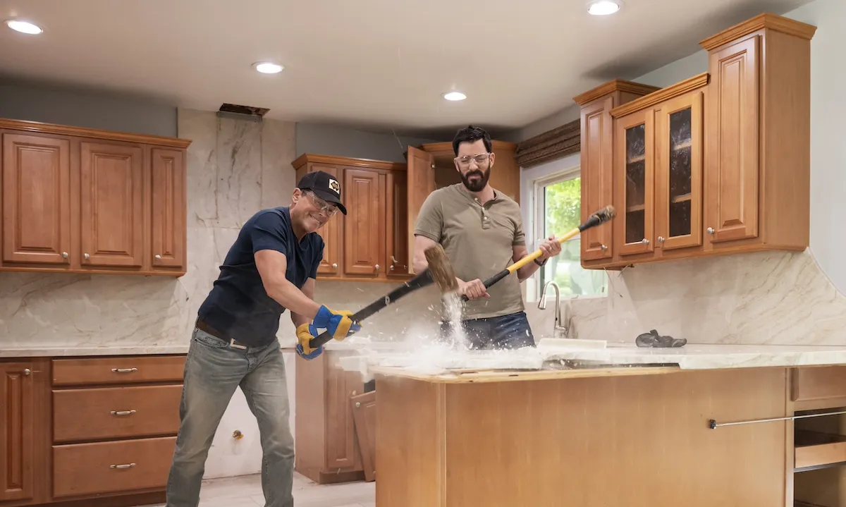 Rob Lowe smashes a countertop with a sledgehammer as one of the Property Brothers looks on