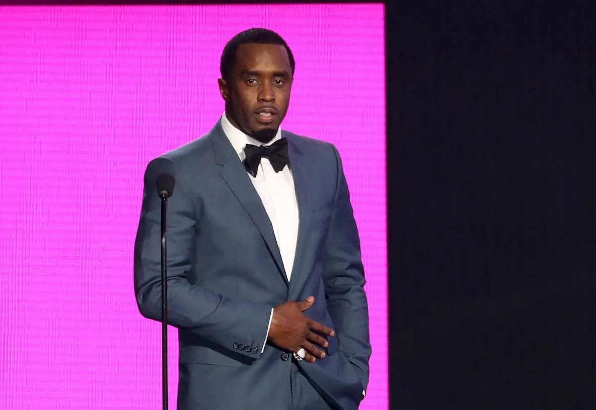 Sean 'Diddy' Combs wears a tuxedo and stands in front of a pink screen.