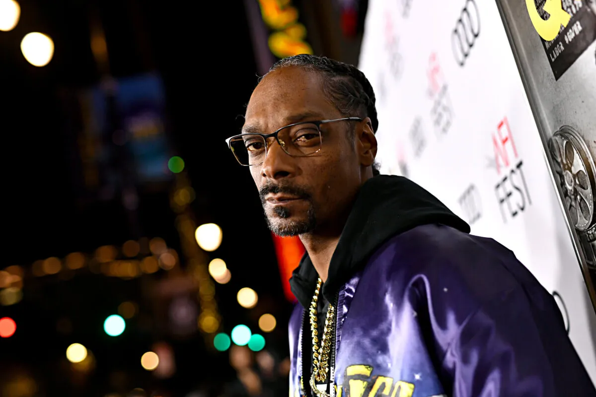 Snoop Dogg wears glasses and a blue jacket over a hoodie.