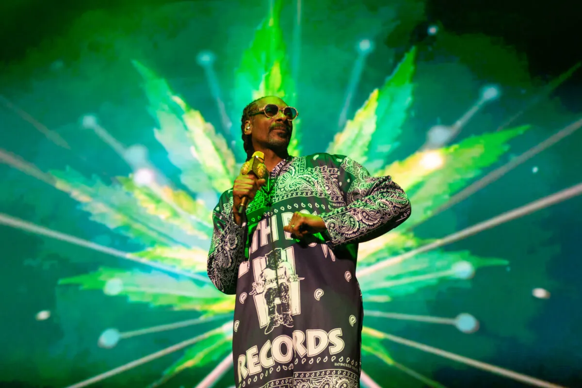 Snoop Dogg wears sunglasses and holds a microphone. He stands in front of the graphic of a marijuana leaf.