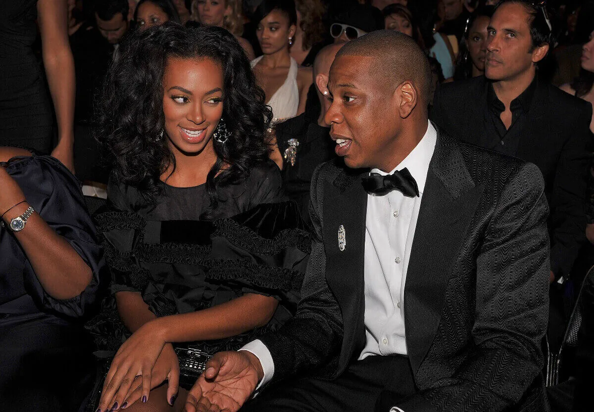 Solange Knowles and Jay-Z wear black and sit together at the Academy Awards. They smile.