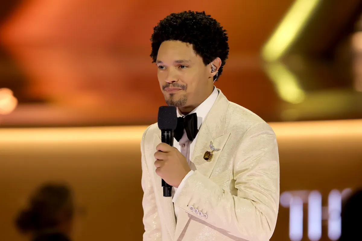 Trevor Noah in a white jacket and holding a microphone