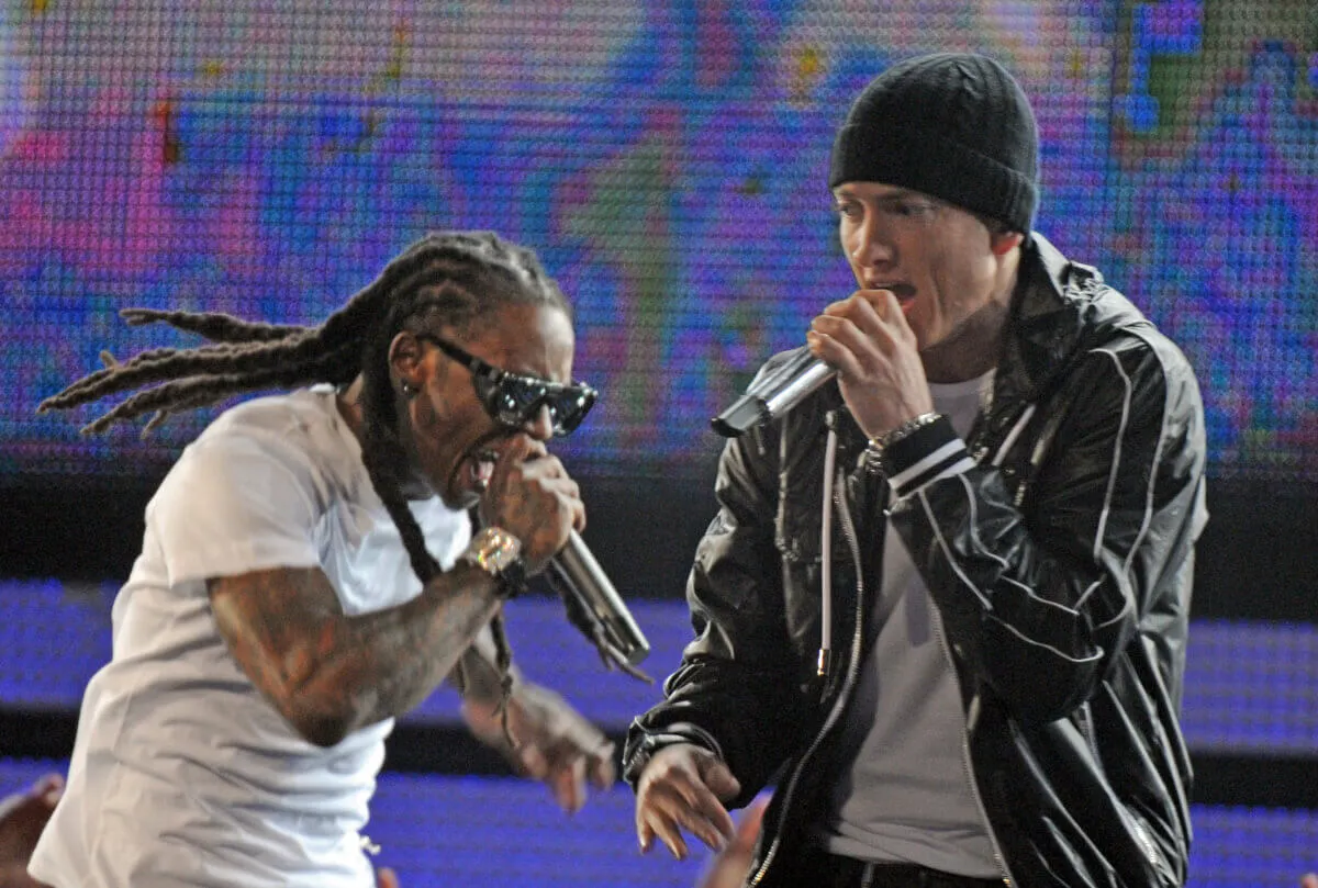 Lil Wayne and Eminem both hold microphones while on a stage together.