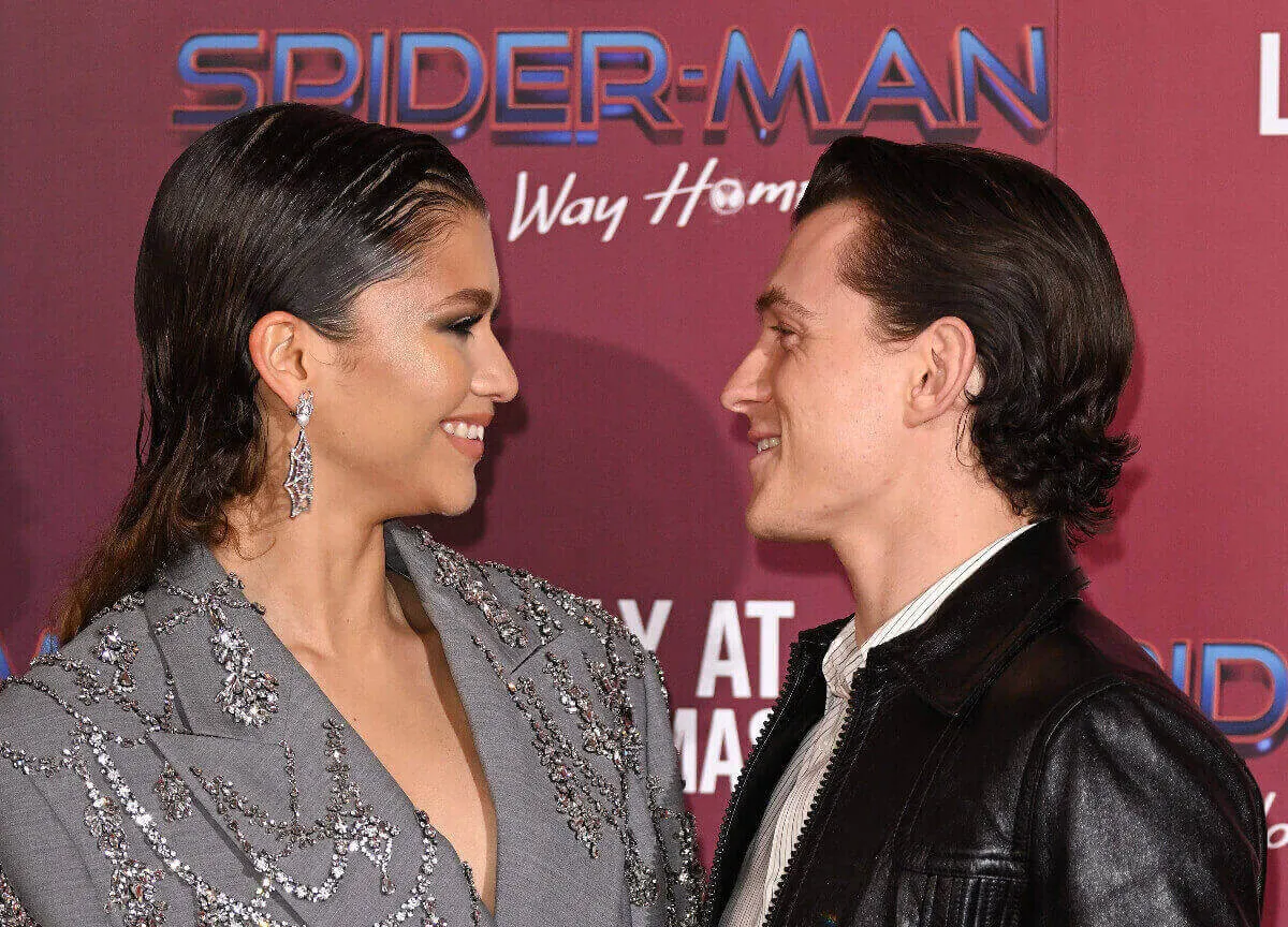 Zendaya wears silver and stares at Tom Holland, who wears black. They smile.