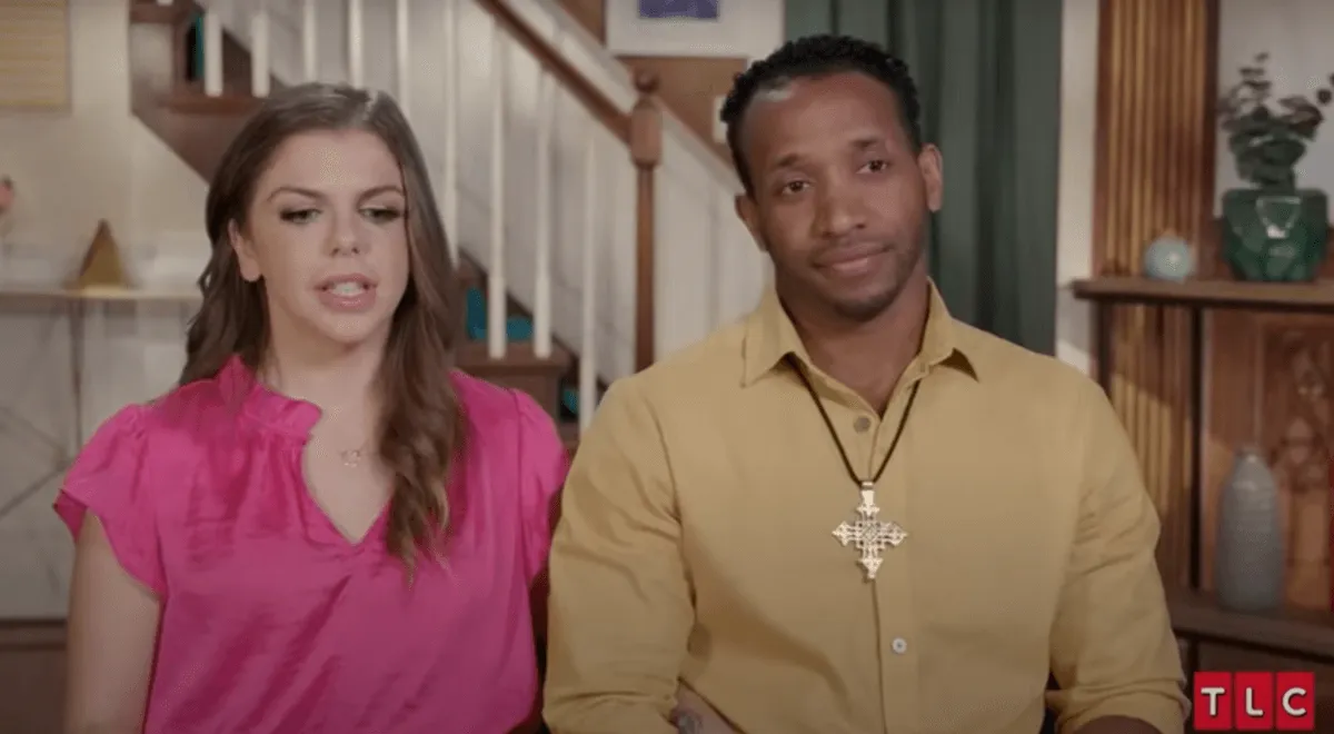 Ari, in a pink shirt, sits next to her husband Bini in an episode of '90 Day Fiance'