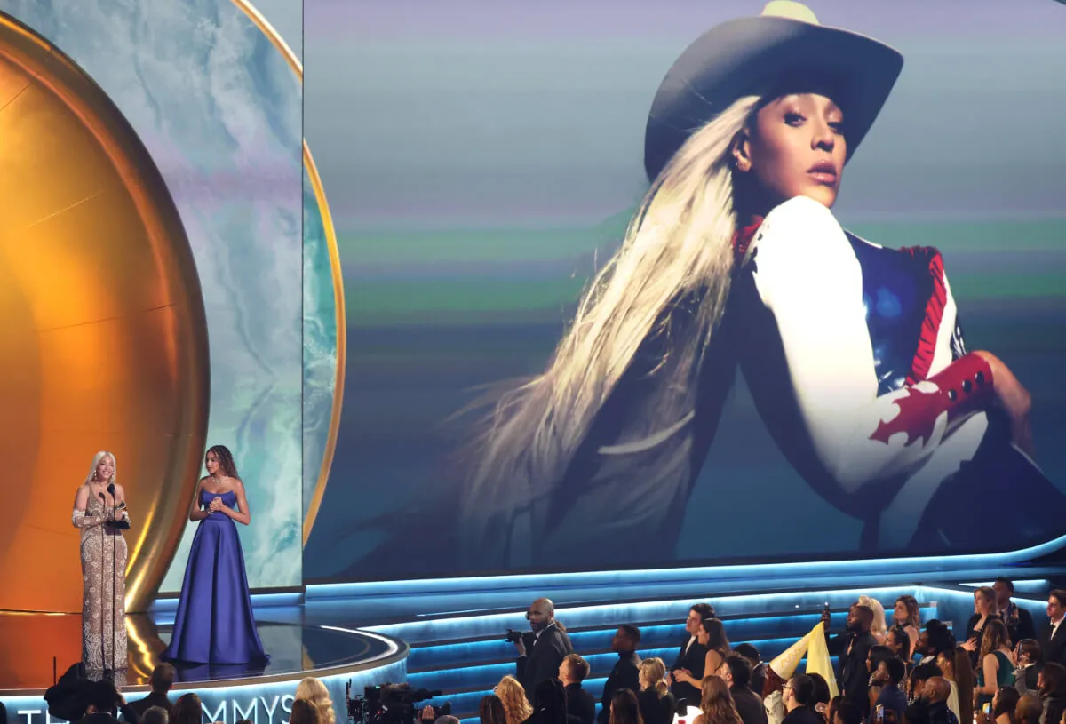 Beyonce and her daughter, Blue Ivy stand on stage at the Grammys. A large photo of her in a cowboy hat is above them.