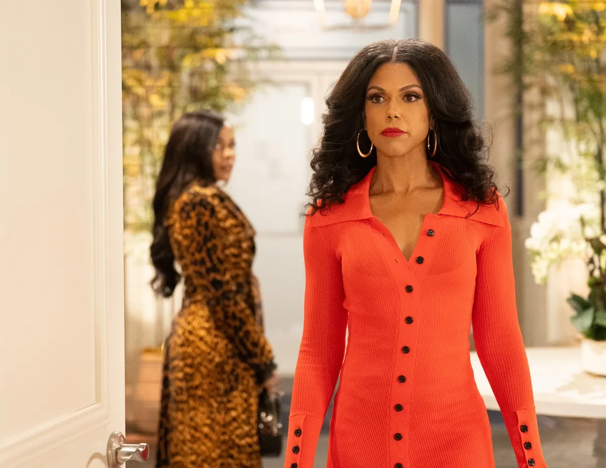 A woman with long curly hair and wearing an orange button-down dress in 'Beyond the Gates'