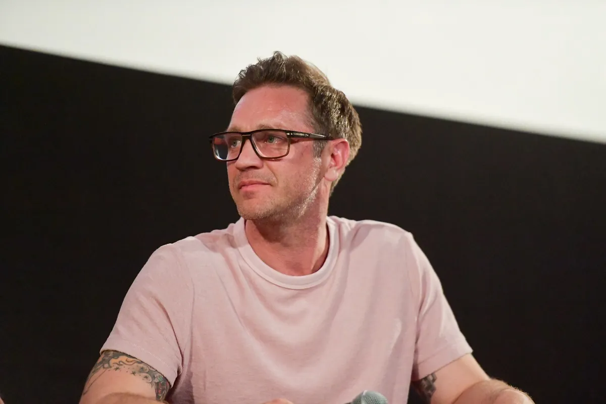 Devon Sawa speaks onstage during the premiere of Quiver Distribution's "The Fanatic" in a pink shirt and glasses.