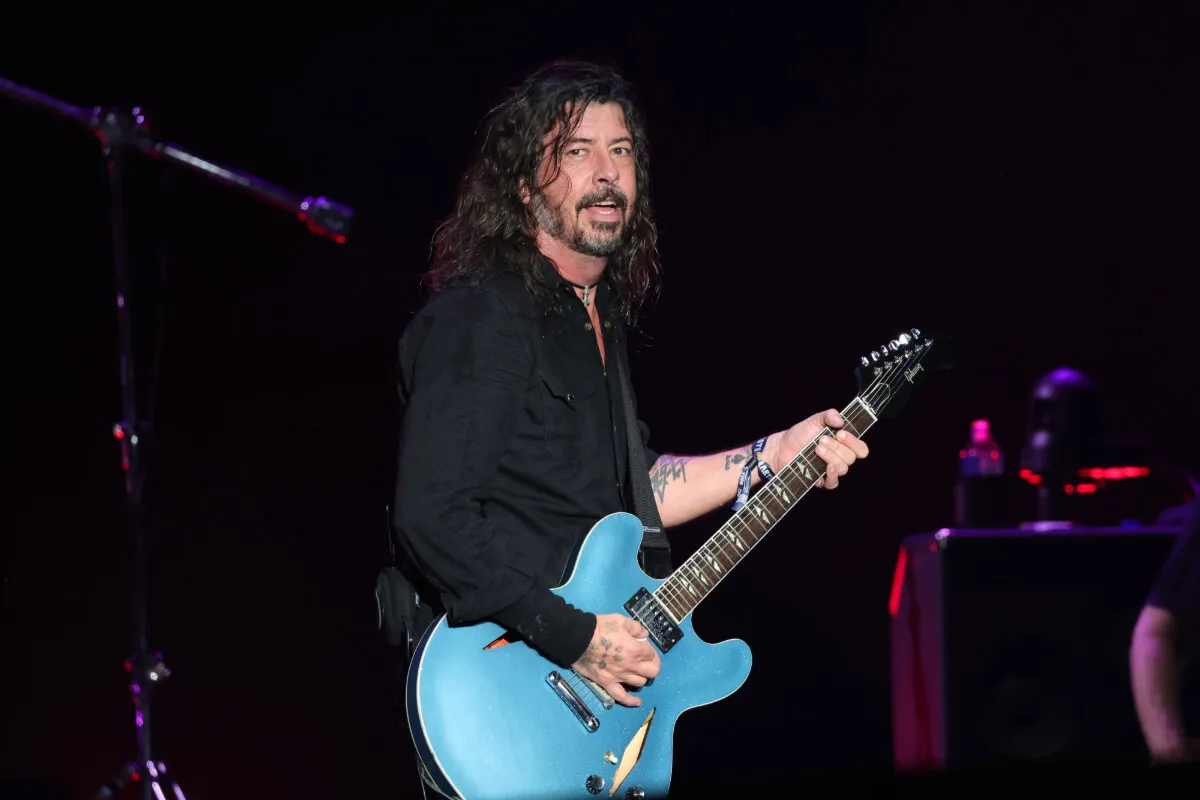 Dave Grohl wears a black shirt and holds a blue guitar.