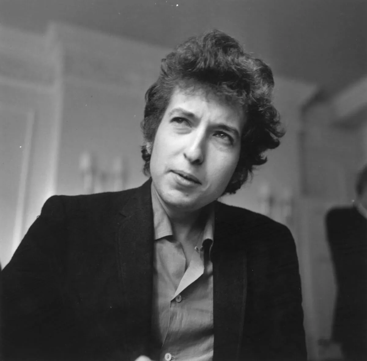 A black and white picture of of Bob Dylan wearing a collared shirt and jacket.