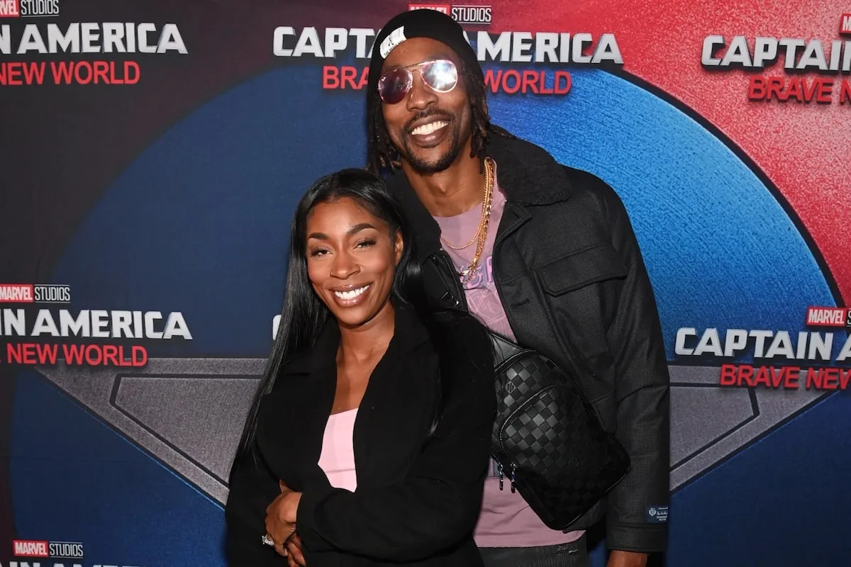 Wearing matching black jackets and pink tops, Dwight Howard and Amy Luciani take photos together on the red carpet before a movie screening