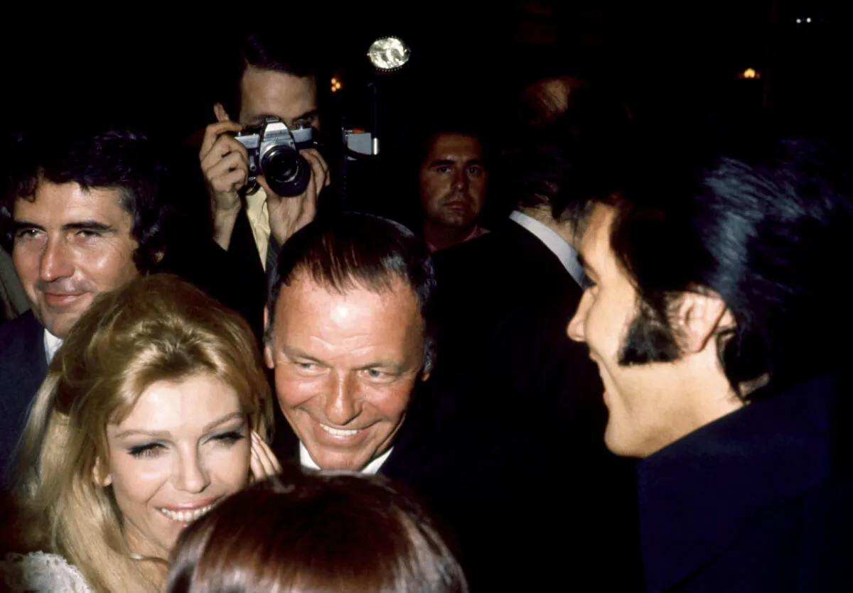 Nancy and Frank Sinatra stand in a crowd facing Elvis Presley. 