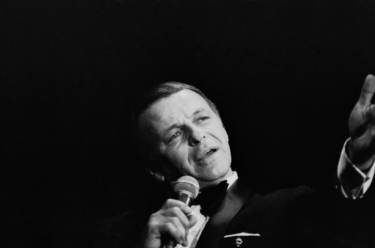 A black and white picture of Frank Sinatra wearing a suit and singing into a microphone.