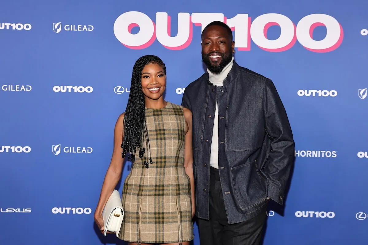 Wearing a plaid mini dress, Gabrielle Union smiles with Dwyane Wade at a media event in 2024