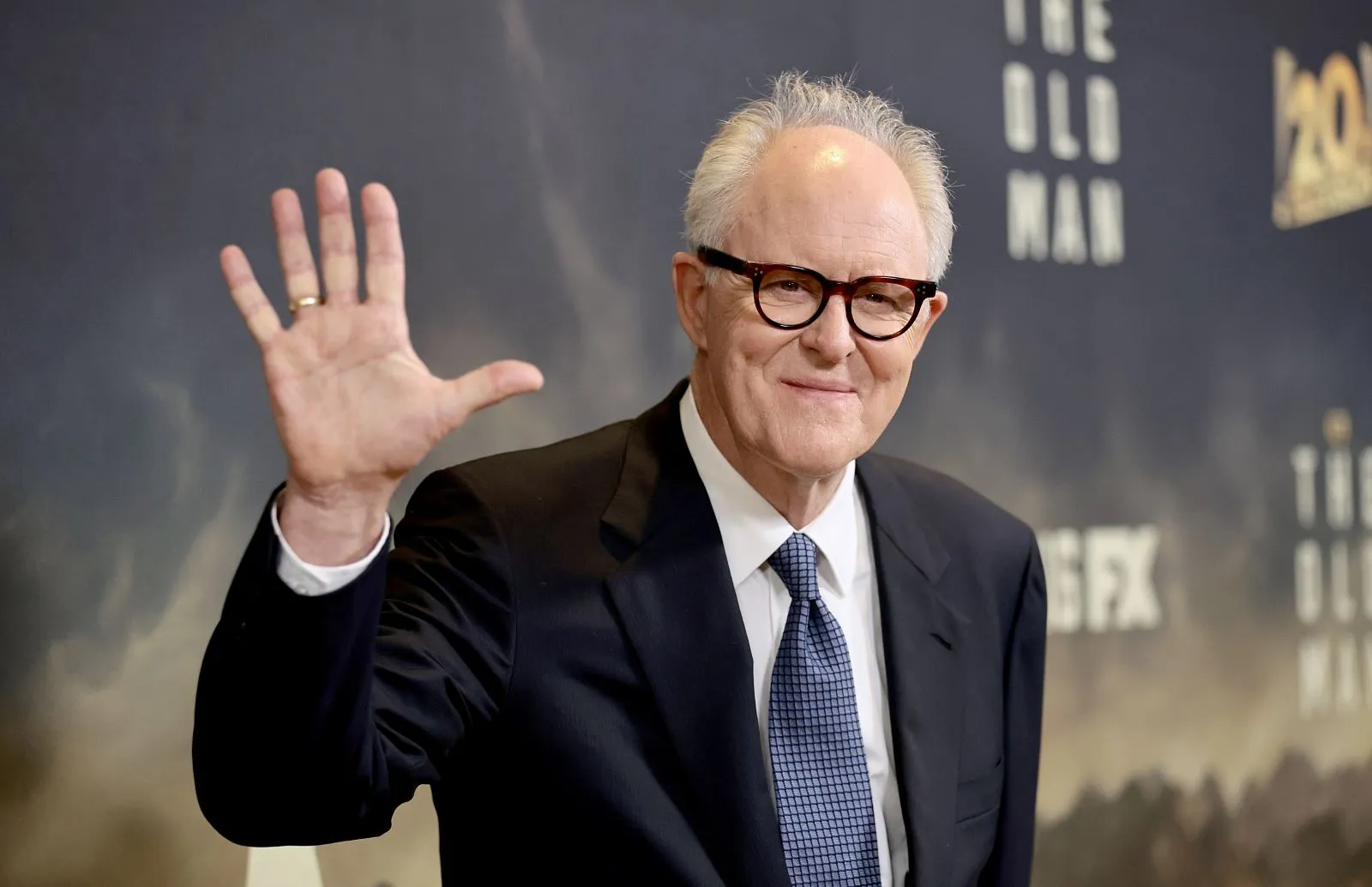 Potential Dumbledore actor John Lithgow waves wearing a suit.