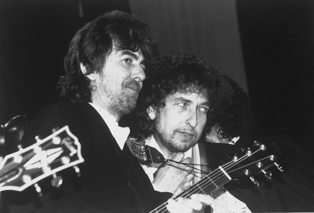 A black and white picture of George Harrison and Bob Dylan standing together while holding guitars.