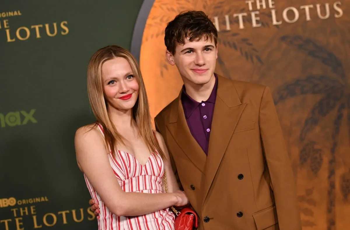 Wearing a brown suit, Sam Nivola smiles with his girlfriend Iris Apatow at the season 3 premiere of HBO's 'The White Lotus'