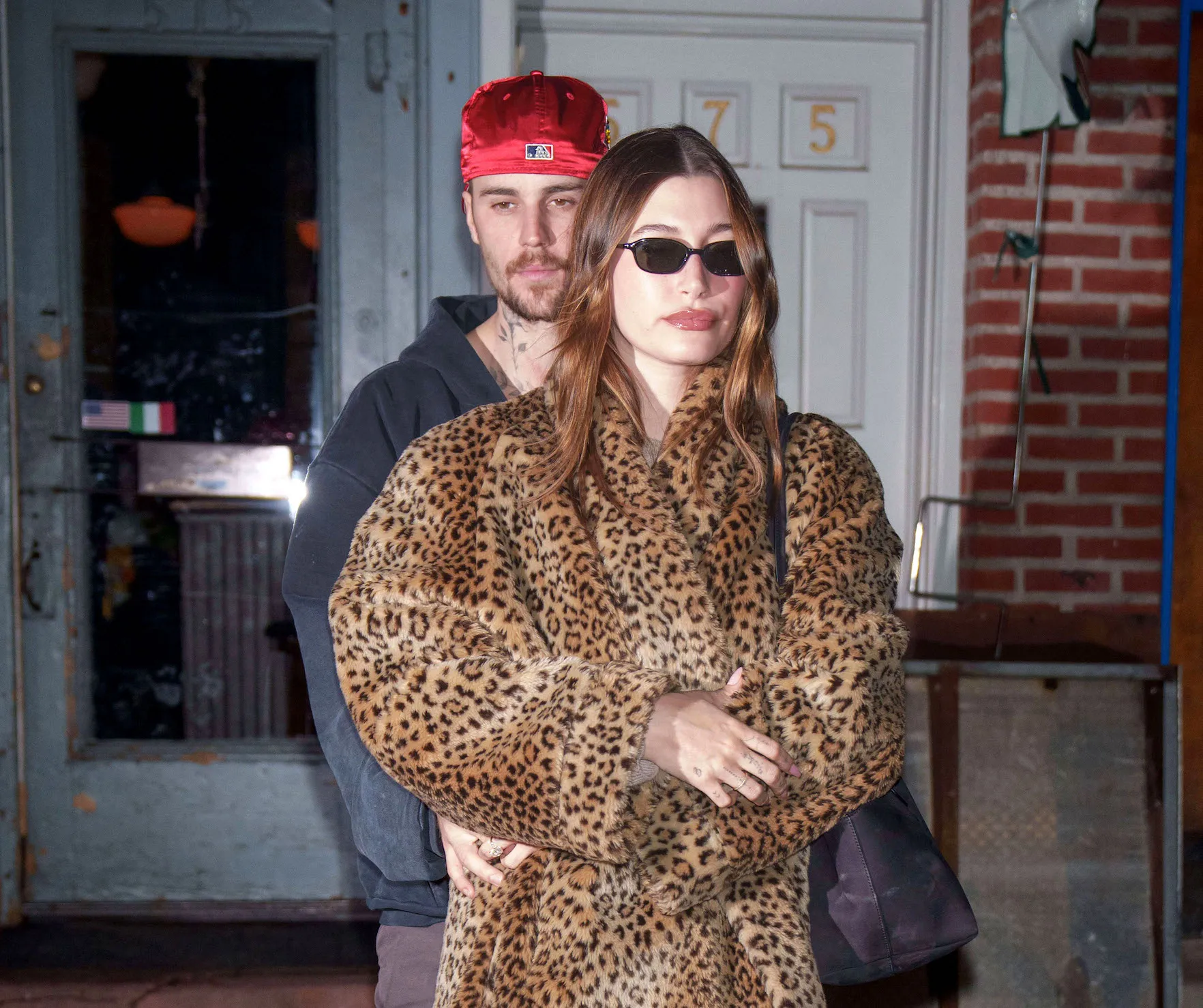 Justin Bieber standing behind Hailey Bieber at night in New York City. Hailey is wearing a leopard-print coat.