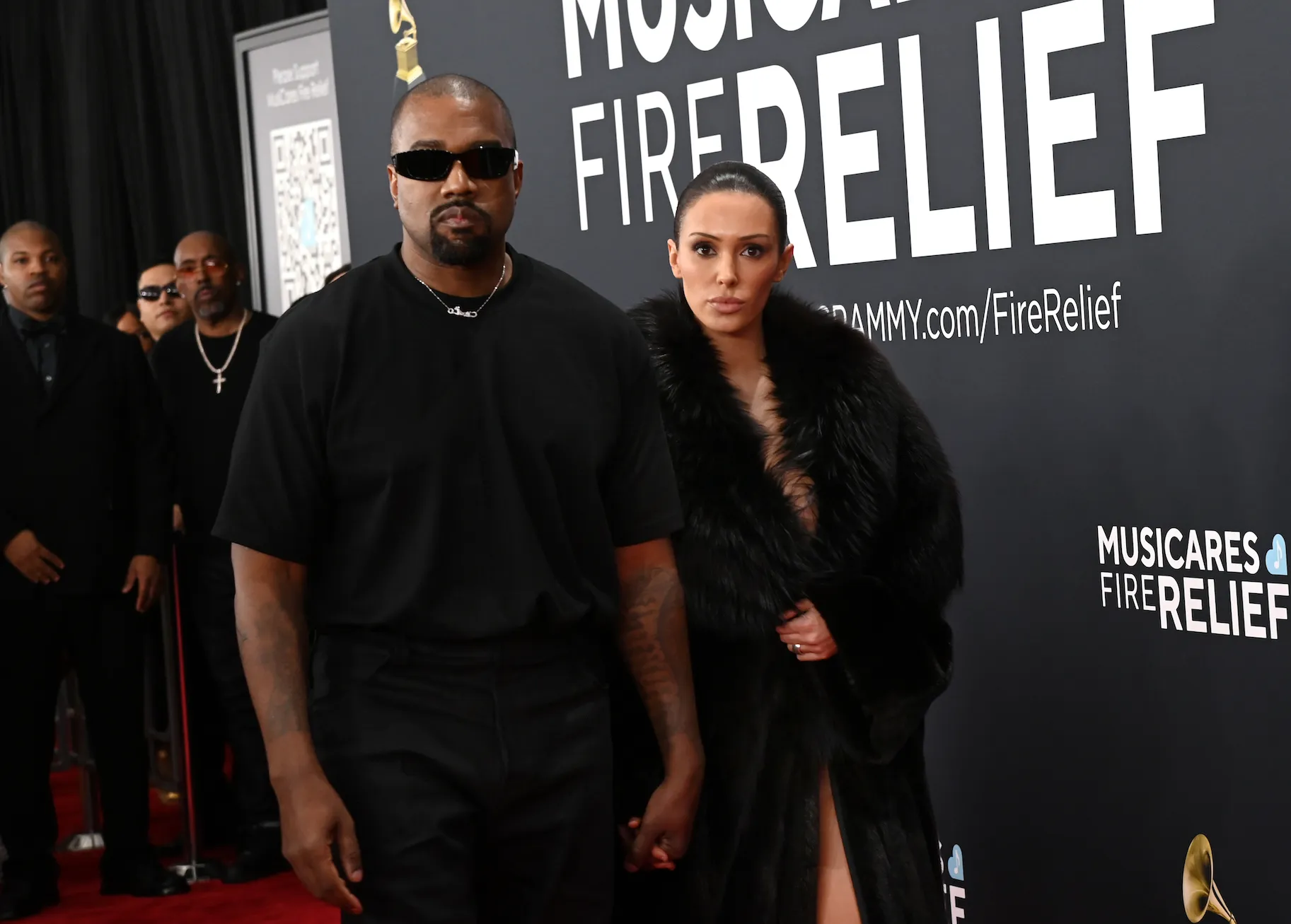 Kanye West in all black walking hand in hand with Bianca Censori in a fur coat on the red carpet