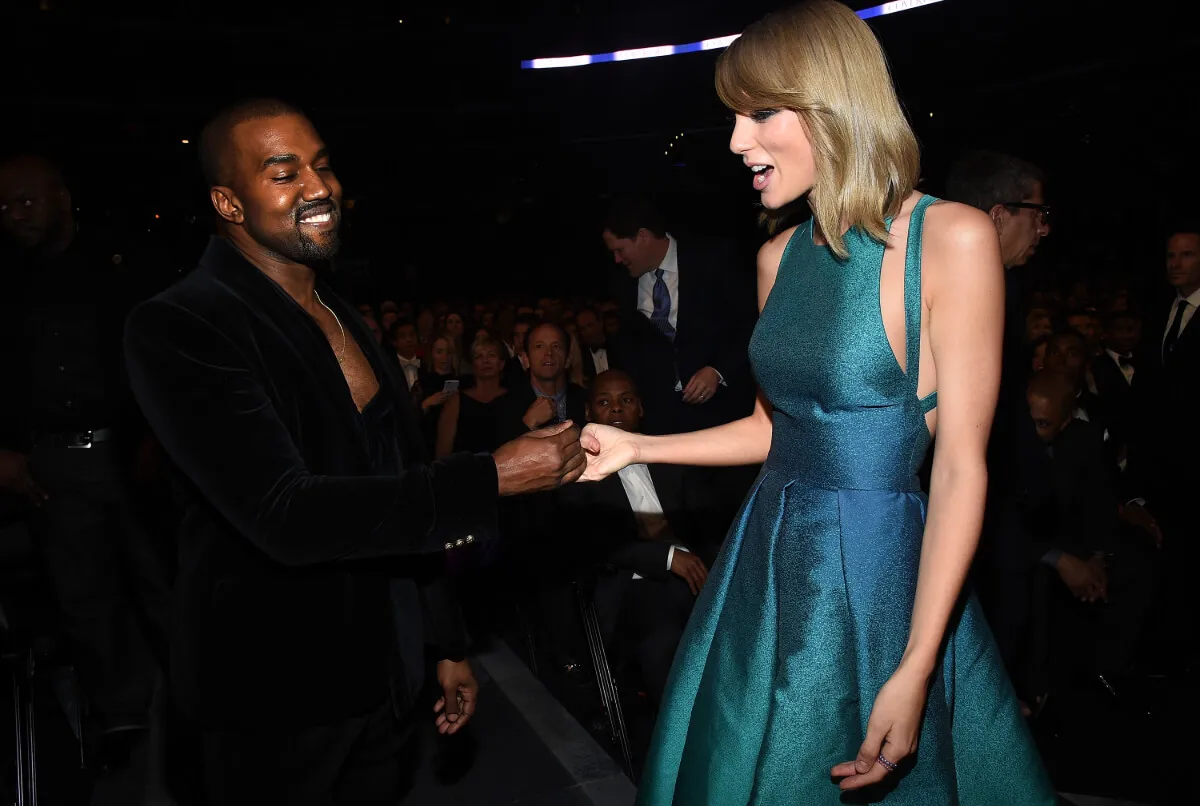 Kanye West wears a black suit and touches Taylor Swift's hand. She wears a teal dress.