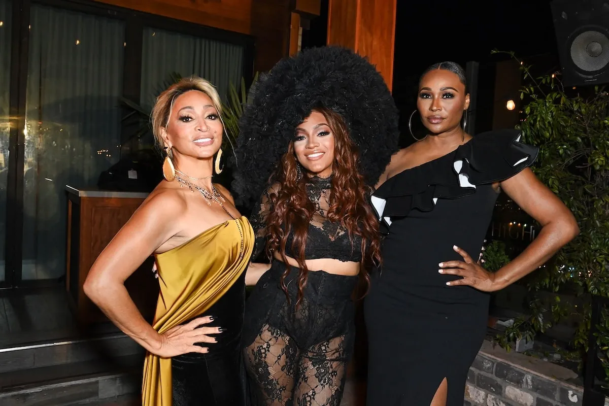 Wearing a yellow and black gown, Karen Huger smiles with Drew Sidora and Cynthia Bailey at a media event in 2024