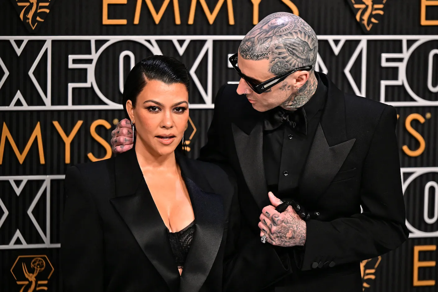 Kourtney Kardashian standing next to Travis Barker, who's looking down at her, at the 75th Emmy Awards. They are both dressed in black.