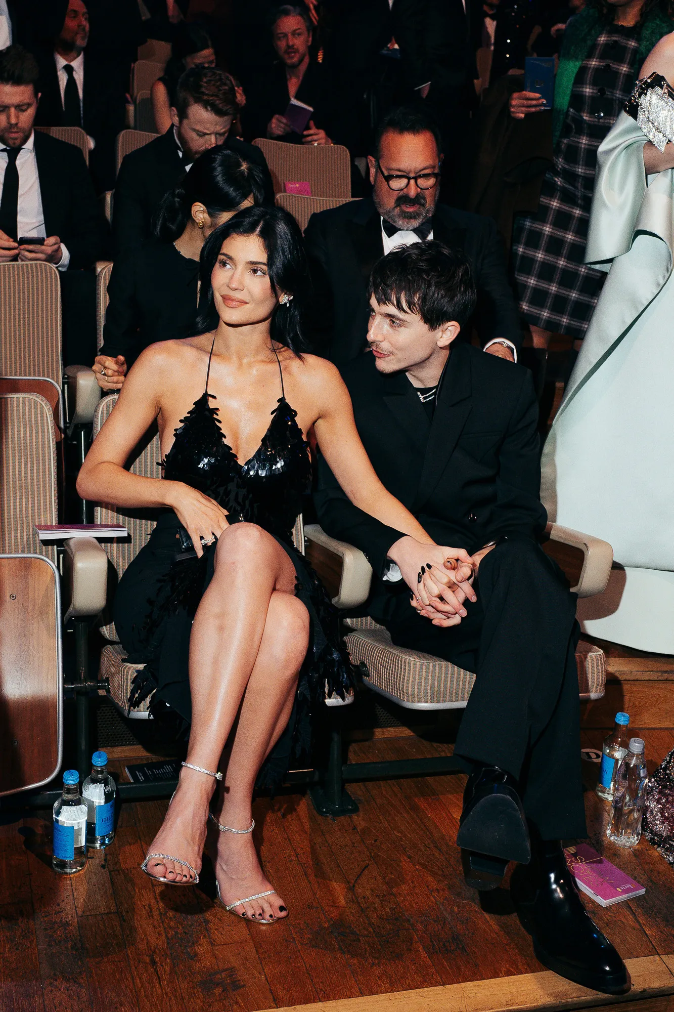 Kylie Jenner and Timothée Chalamet sitting with each other at the BAFTAs. They're holding hands and dressed up.