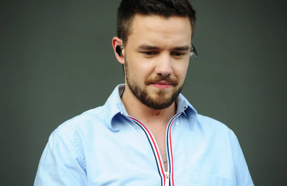 Liam Payne wears a blue collared shirt and wears earphones.