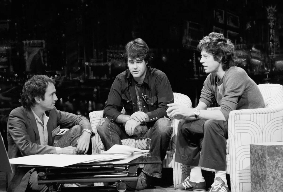 A black and white picture of Lorne Michaels sitting with Dan Aykroyd and Mick Jagger on SNL.