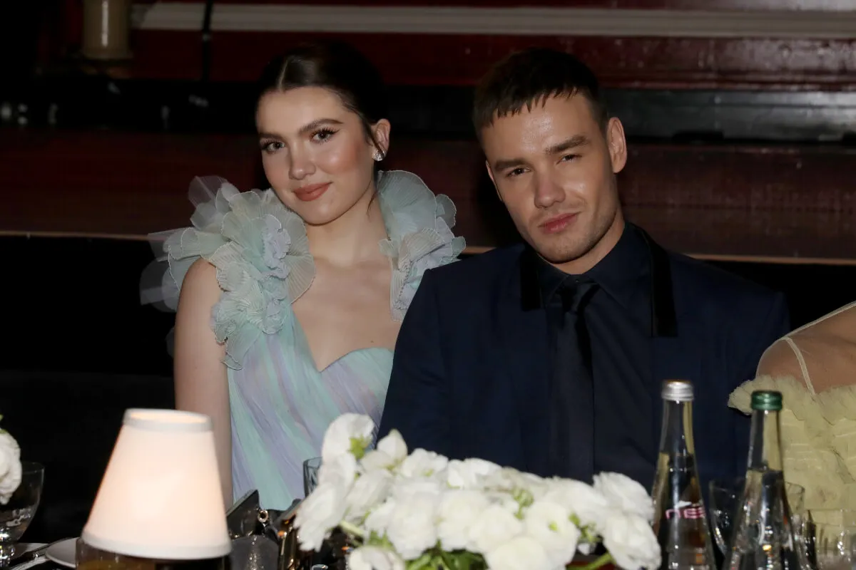 Maya Henry wears a blue dress and sits next to Liam Payne, who wears a black suit.