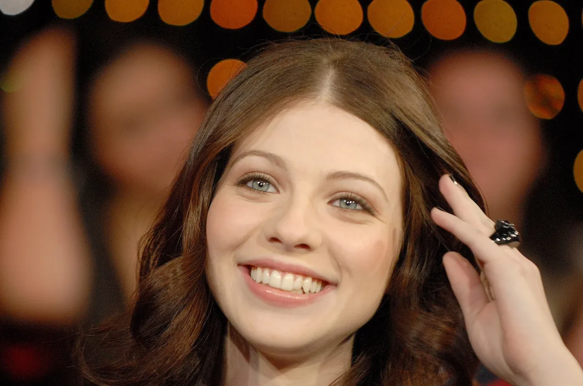 Smiling Michelle Trachtenberg brushing her brown hair from her face