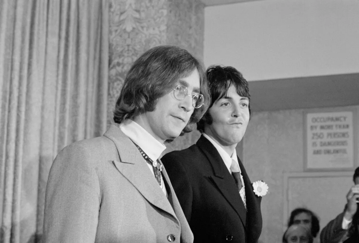 A black and white picture of John Lennon and Paul McCartney standing together wearing suits.