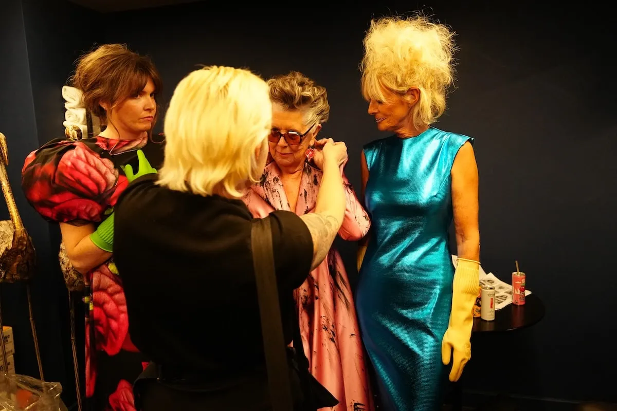 Models Hannah Rogers, Dame Prue Leith, and Jane Moore adjust their accessories backstage ahead of the VIN + OMI London runway show