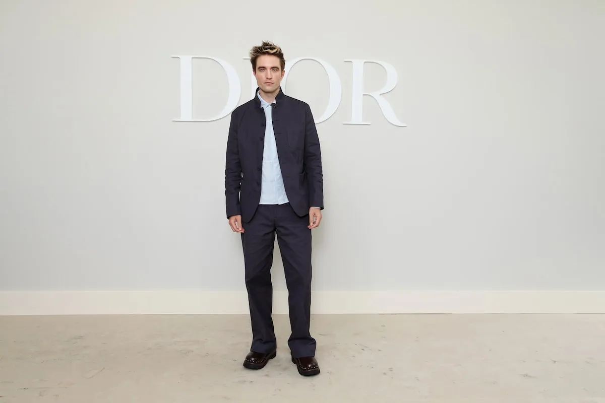 Wearing a gray jacket and pants, Robert Pattinson looks at cameras at the Dior Homme Menswear Spring/Summer 2025 show