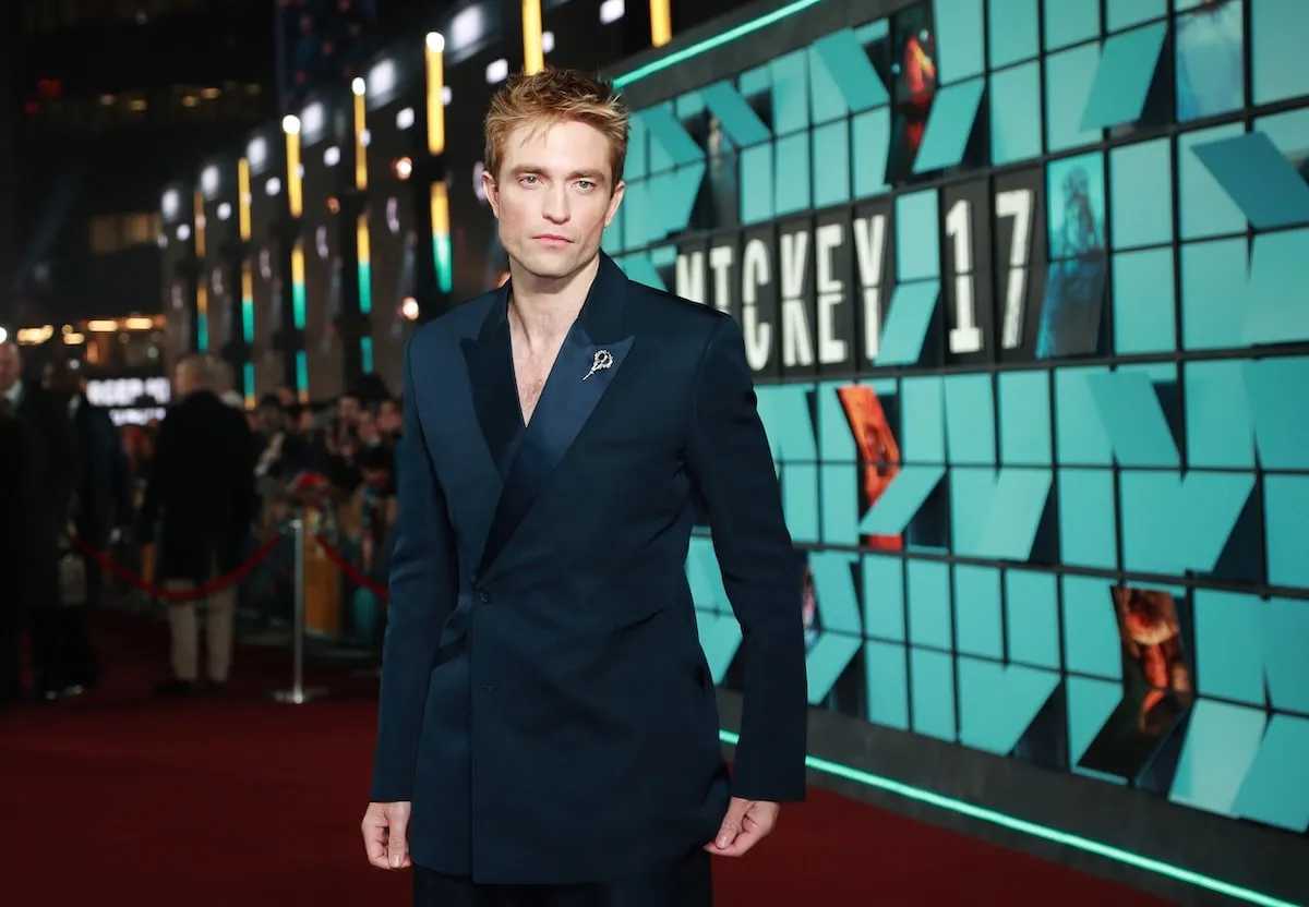 Wearing a navy tuxedo and gold lapel pin, Robert Pattinson poses for cameras at the world premiere of 'Mickey 17'