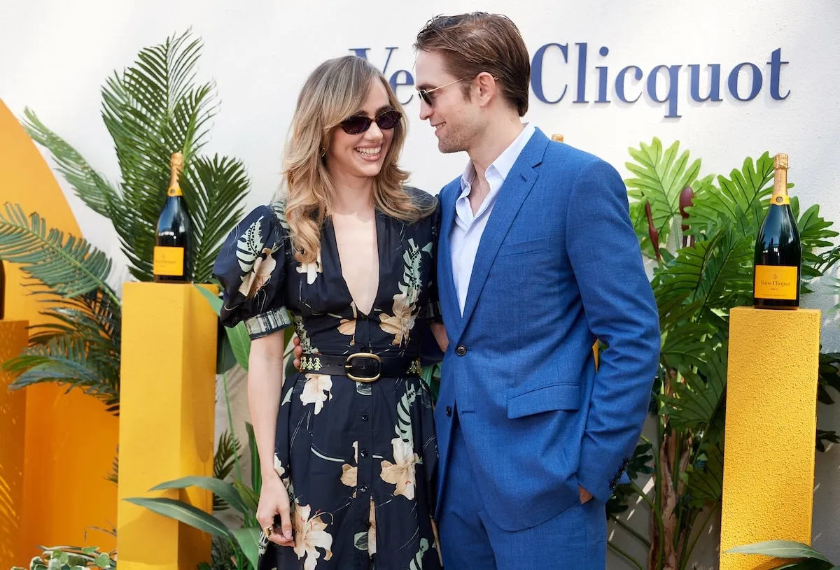 Standing in front of yellow champagne bottles, English celebrities Robert Pattinson and Suki Waterhouse laugh together at the Veuve Clicquot Polo Classic in 2024