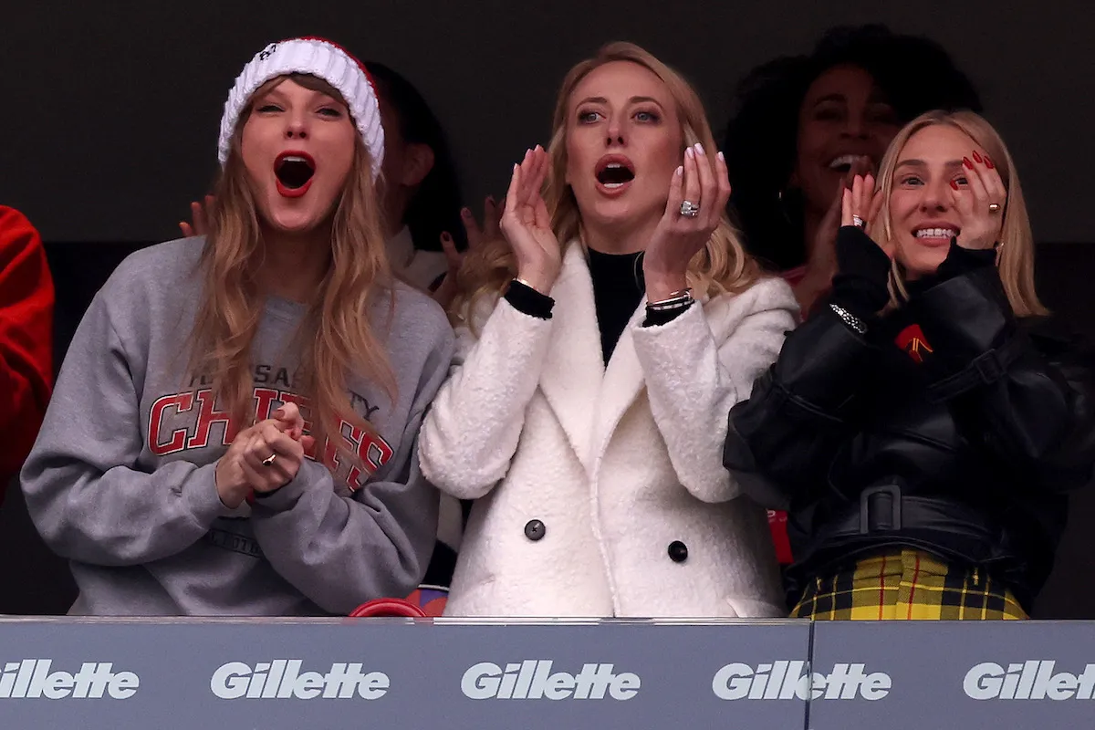 Taylor Swift, Brittany Mahomes, and Ashley Avignone cheering and clapping in the stands of a Kansas City Chiefs game