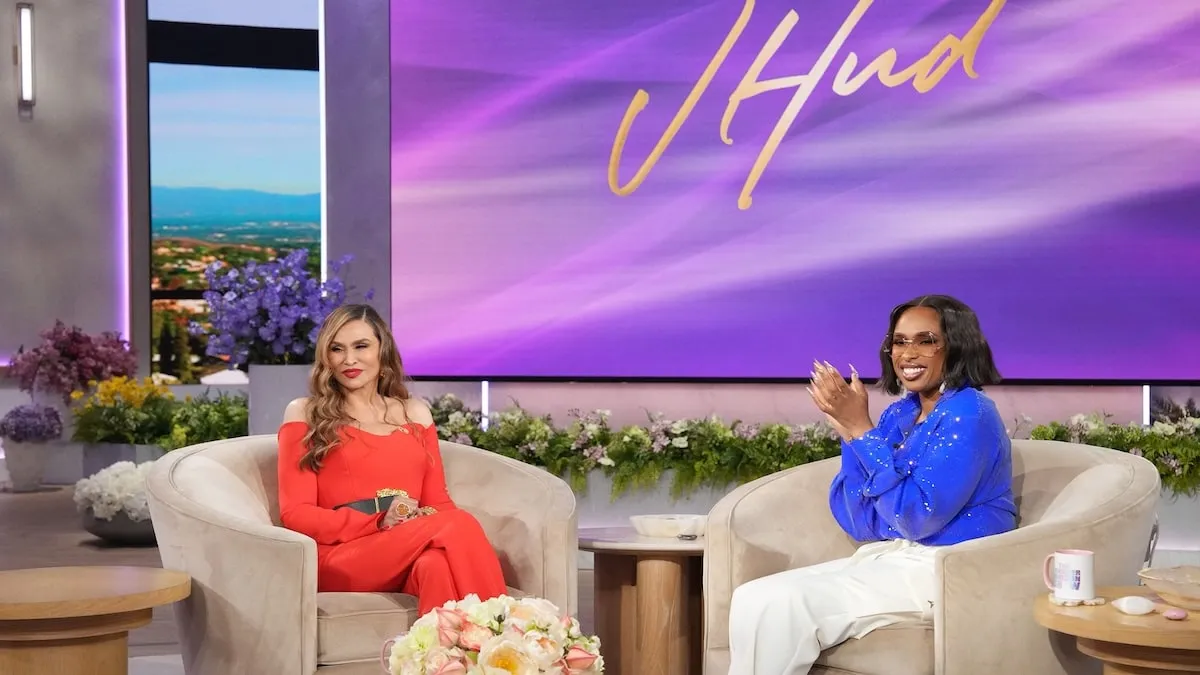 Wearing a red jumpsuit, Tina Knowles smiles at the audience on The Jennifer Hudson Show