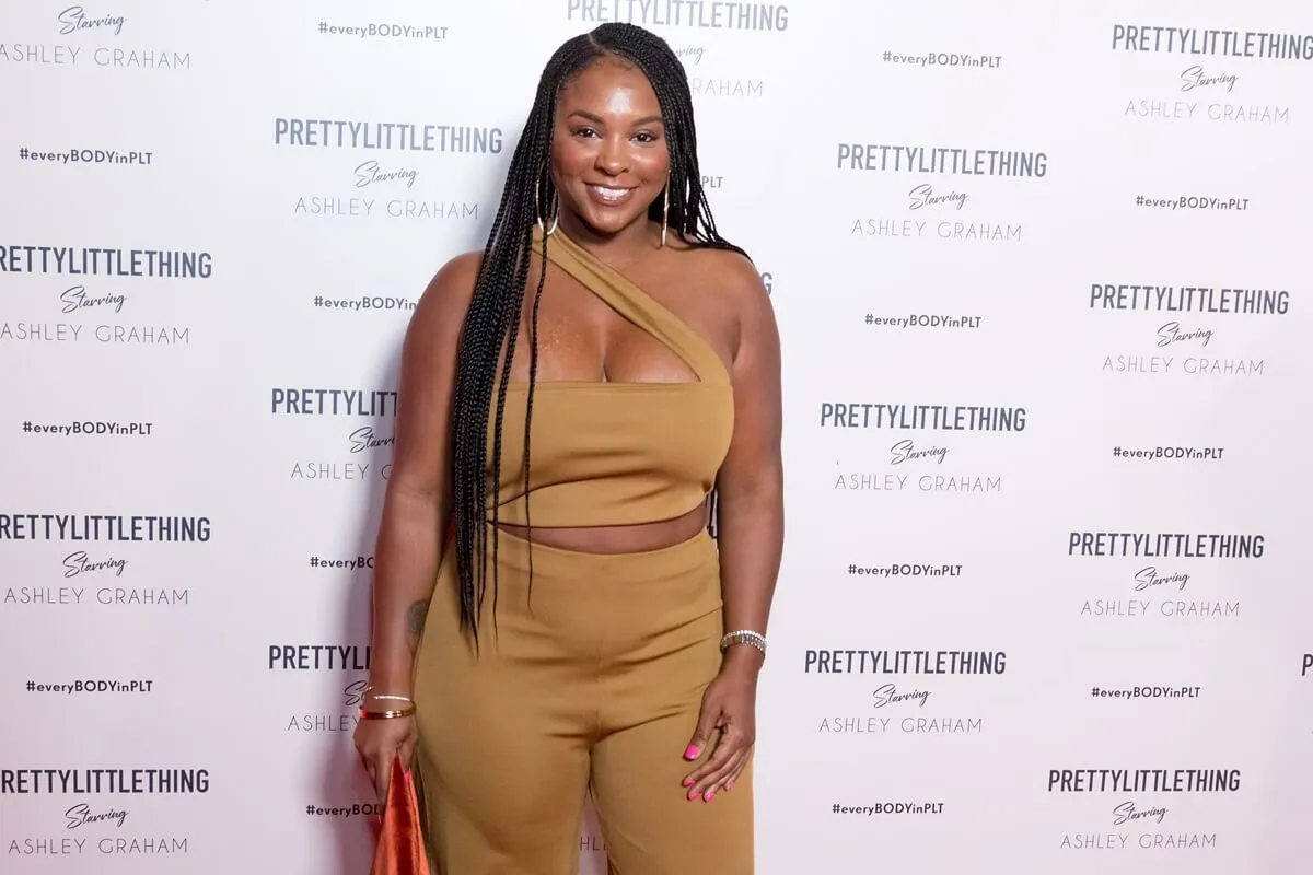 Torrei Hart posing at the PrettyLittleThing x Ashley Graham Event at Delilah in a brown dress.