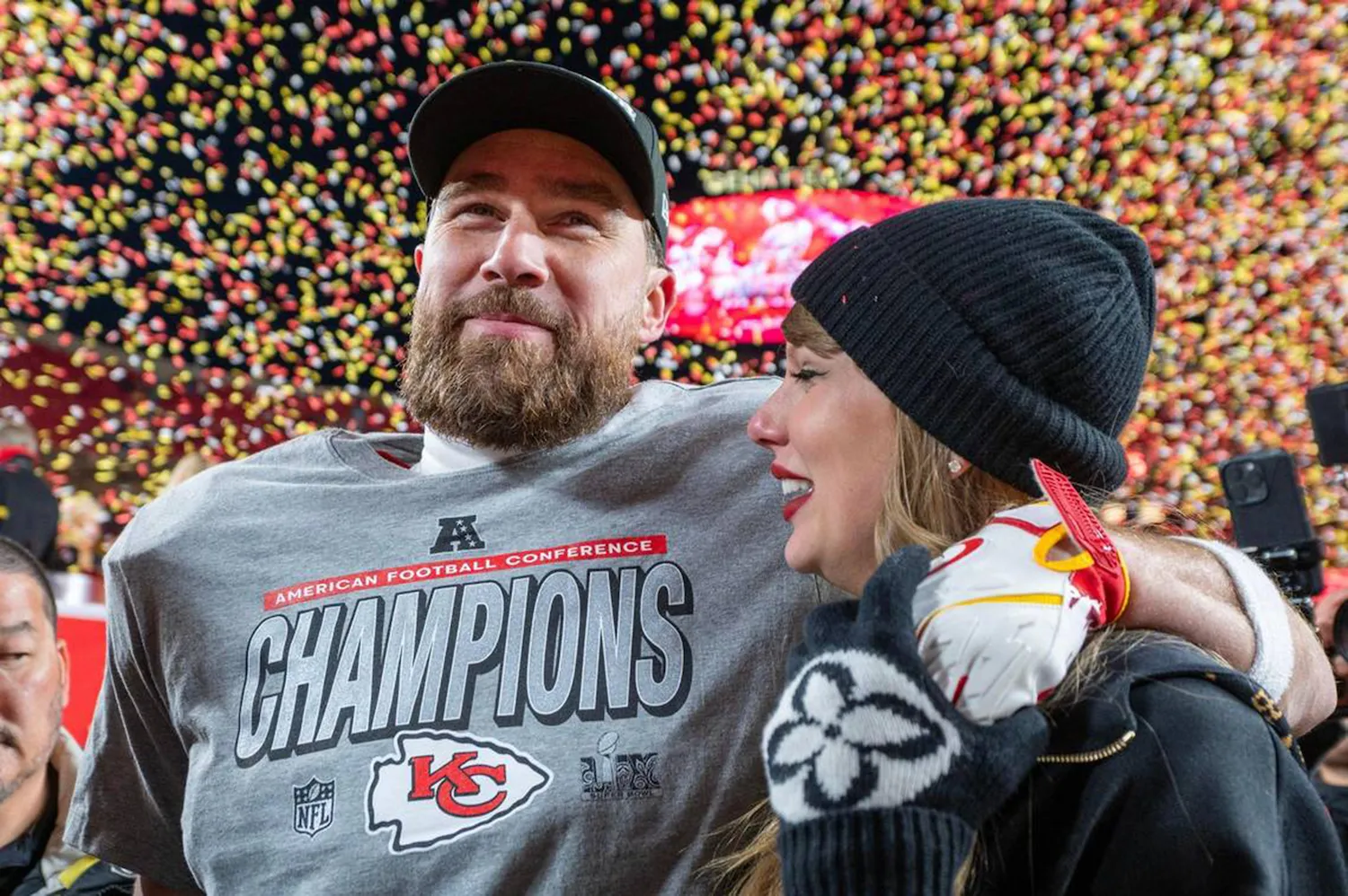 Travis Kelce smiling as Taylor Swift smiles and leans into him after a Kansas City Chiefs win. Confetti is in the background.