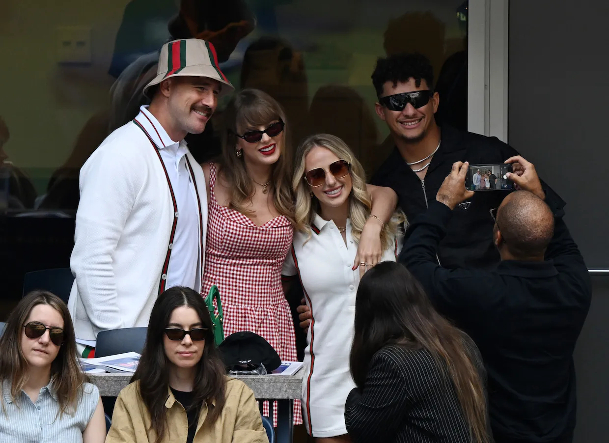 Travis Kelce, Taylor Swift, Brittany Mahomes, and Patrick Mahomes standing and smiling with their arms around each other at the US Open.