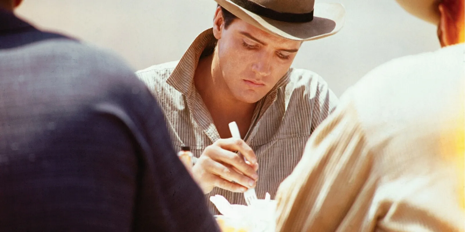 Elvis Presley sitting at a picnic table and ready to eat on location for the 20th Century Fox western, 'Flaming Star', directed by Don Siegel, 1960