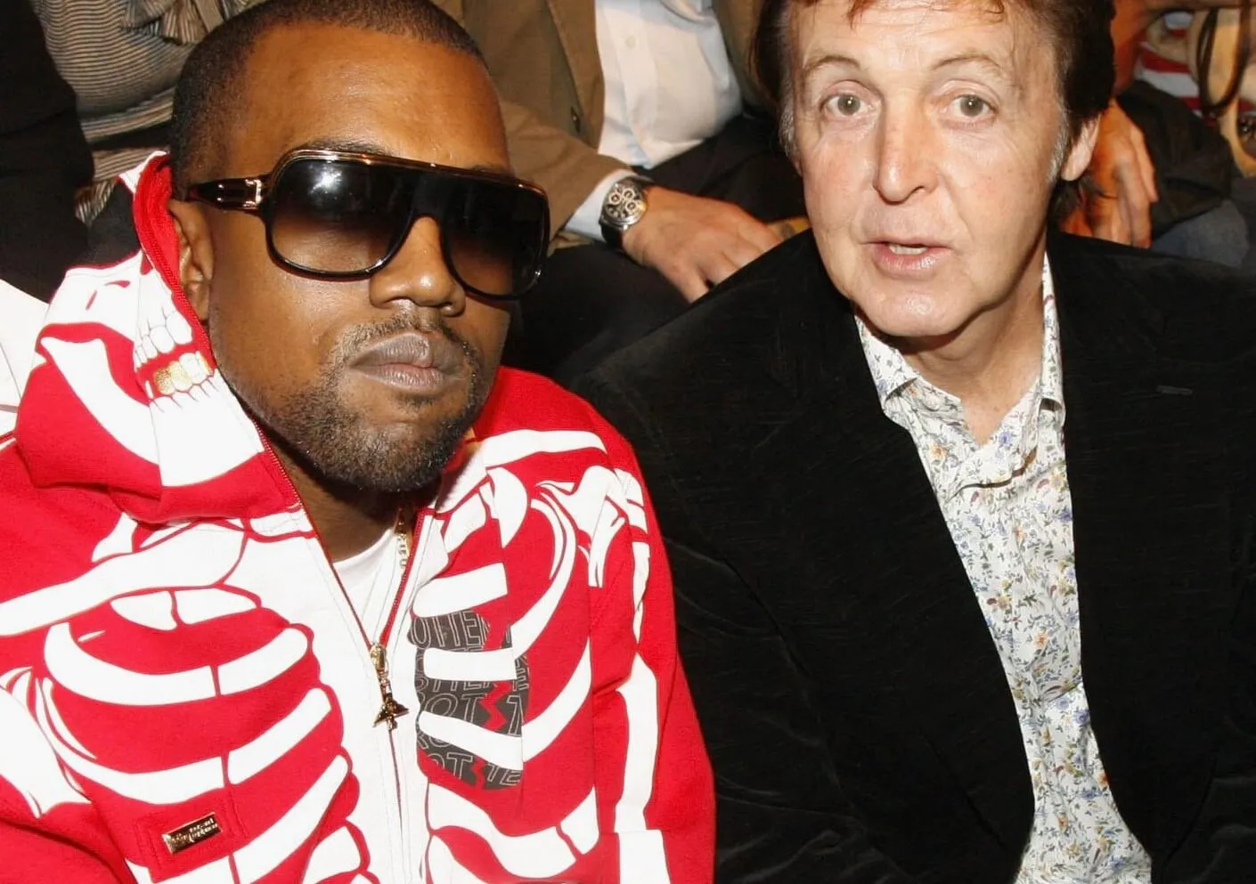 Kanye West next to The Beatles' Paul McCartney. McCartney wears a suit and West wears a red jacket with skeleton pattern and sunglasses.